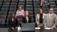 Four invited presenters stand at a hearing table during a Shelby County Commission meeting about the jail health care contract and its oversight provisions.