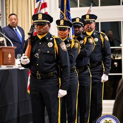 Memphis Police Department color guard members in dress uniforms carrying flags and ceremonial rifles at an indoor ceremony.