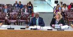 Shelby County Trustee Joseph Lee III speaks into a microphone at a hearing table, with another presenter beside him and attendees seated behind them.