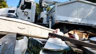 A municipal refuse collection truck parked at a curbside collection site with discarded lumber and bulk debris in the foreground, representing the sanitation workforce covered by the tentative agreement.