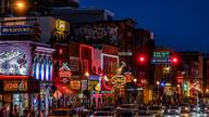 A neon-lit entertainment street at dusk with blurred crowds and unreadable signs.