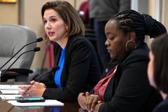 Women seated at a formal hearing table, with one speaking into microphones and another taking notes.