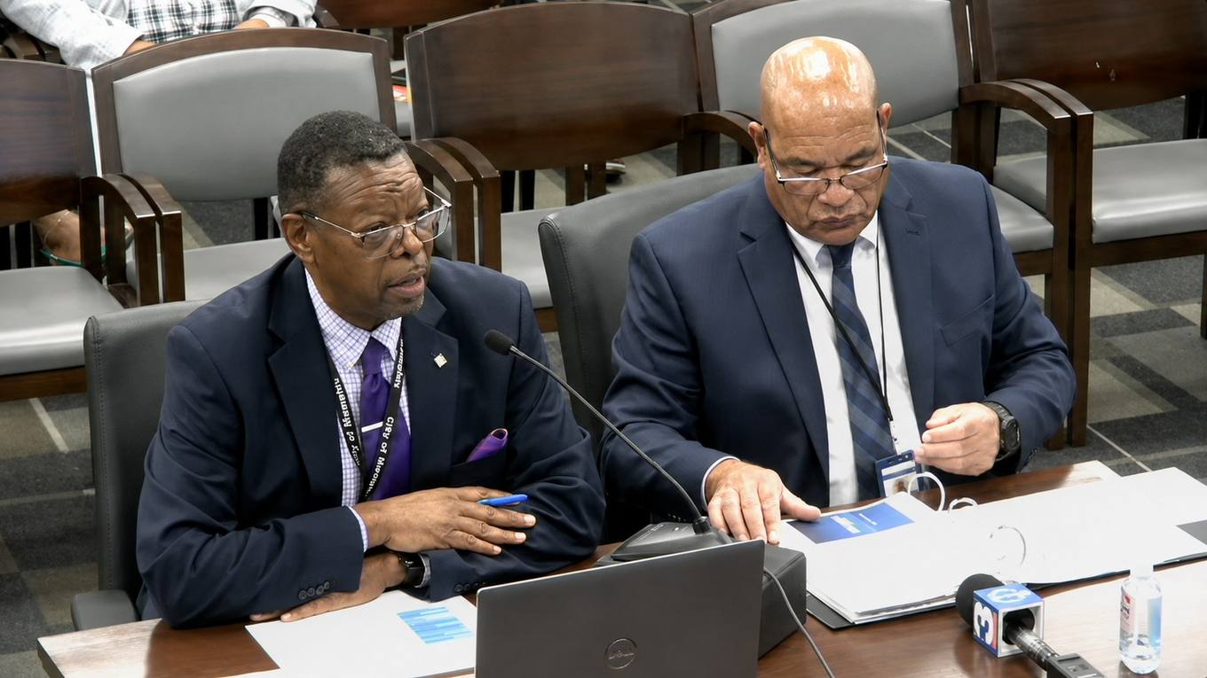 Two City of Memphis officials seated at a witness table with a microphone and documents during a city council committee meeting.