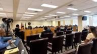 An empty county commission chamber with vacant chairs at the dais after a meeting.