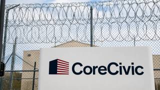 Razor wire tops the perimeter fence of a rural detention facility at dusk.