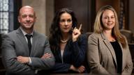 Three attorneys standing in a wood-paneled courtroom, two in suits with arms crossed and one gesturing with a raised finger.