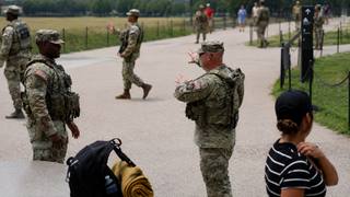 National Guard personnel standing along a walkway on the National Mall in Washington as pedestrians pass.