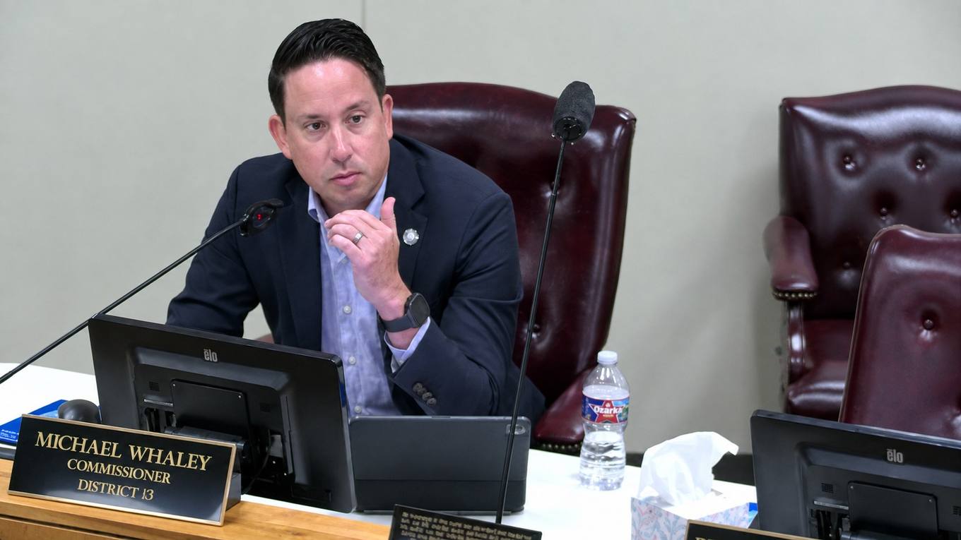 A county commissioner seated at the dais speaking into a microphone during a county budget committee meeting.
