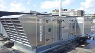 A large rooftop air handling unit on a flat institutional roof under a partly cloudy sky.