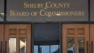 Gold lettering reading Shelby County Board of Commissioners above the wooden doors of the commission chamber.