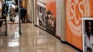 Visitors pass through a metal detector in a Memphis-Shelby County Schools building lobby with a Shelby County Schools mural on the wall.