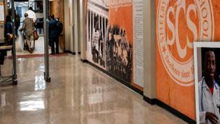 Visitors pass through a metal detector in a Memphis-Shelby County Schools building lobby with a Shelby County Schools mural on the wall.