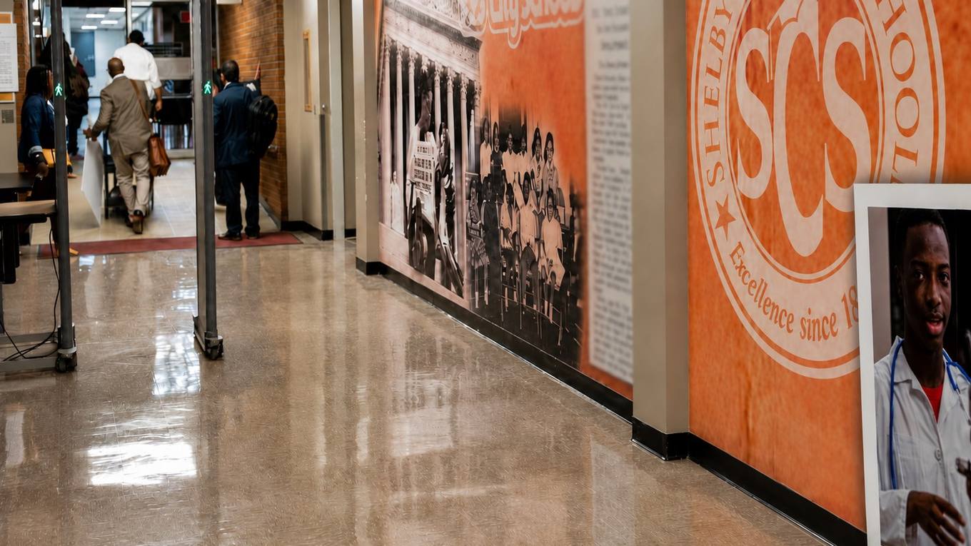 Visitors pass through a metal detector in a Memphis-Shelby County Schools building lobby with a Shelby County Schools mural on the wall.
