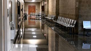 An empty corridor outside the courtrooms at the Shelby County criminal justice complex, with rows of metal benches along a polished stone wall.
