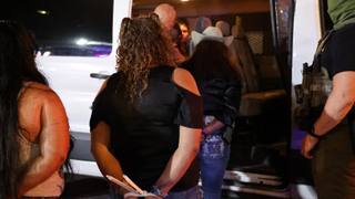People are escorted into a white van by a federal agent during a nighttime immigration enforcement operation at El Corralon on Macon Road in Memphis.