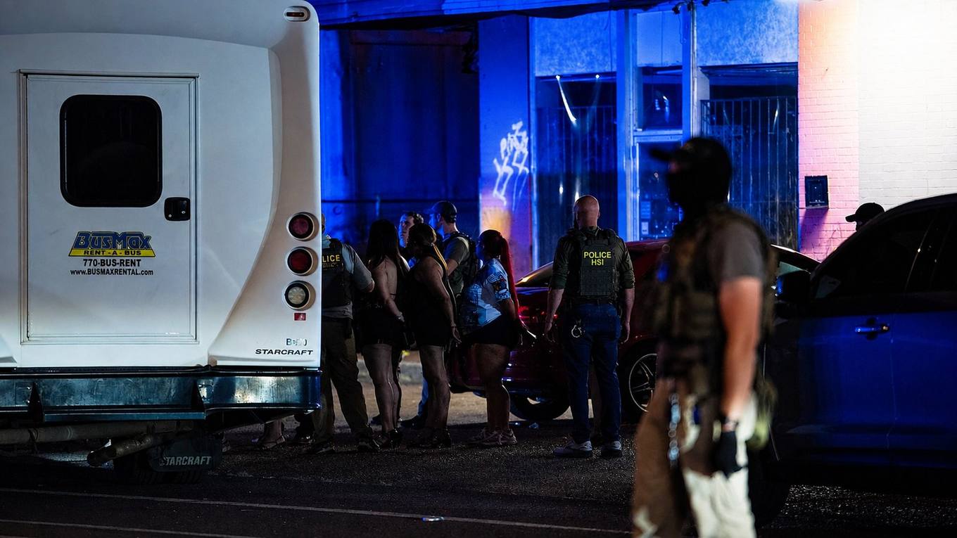 Unmarked buses and government vehicles fill a dark Memphis parking lot before dawn outside a shuttered nightclub.