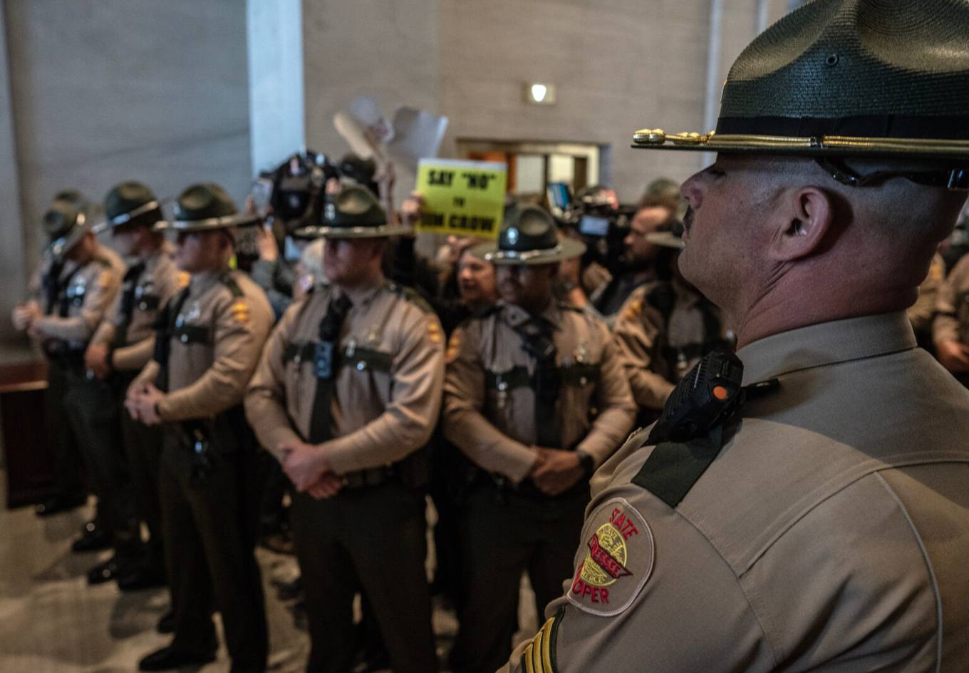 Tennessee State Troopers stand in formation inside the state Capitol as protesters hold a sign reading "Say No to Jim Crow"