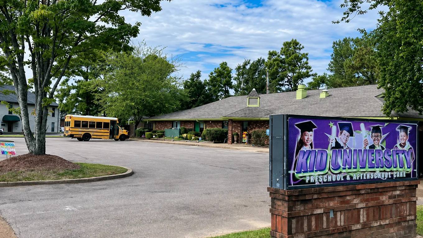 The Kid University childcare center sign and building in Cordova, seen from the parking lot with a small school bus parked outside.