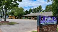 The Kid University childcare center sign and building in Cordova, seen from the parking lot with a small school bus parked outside.