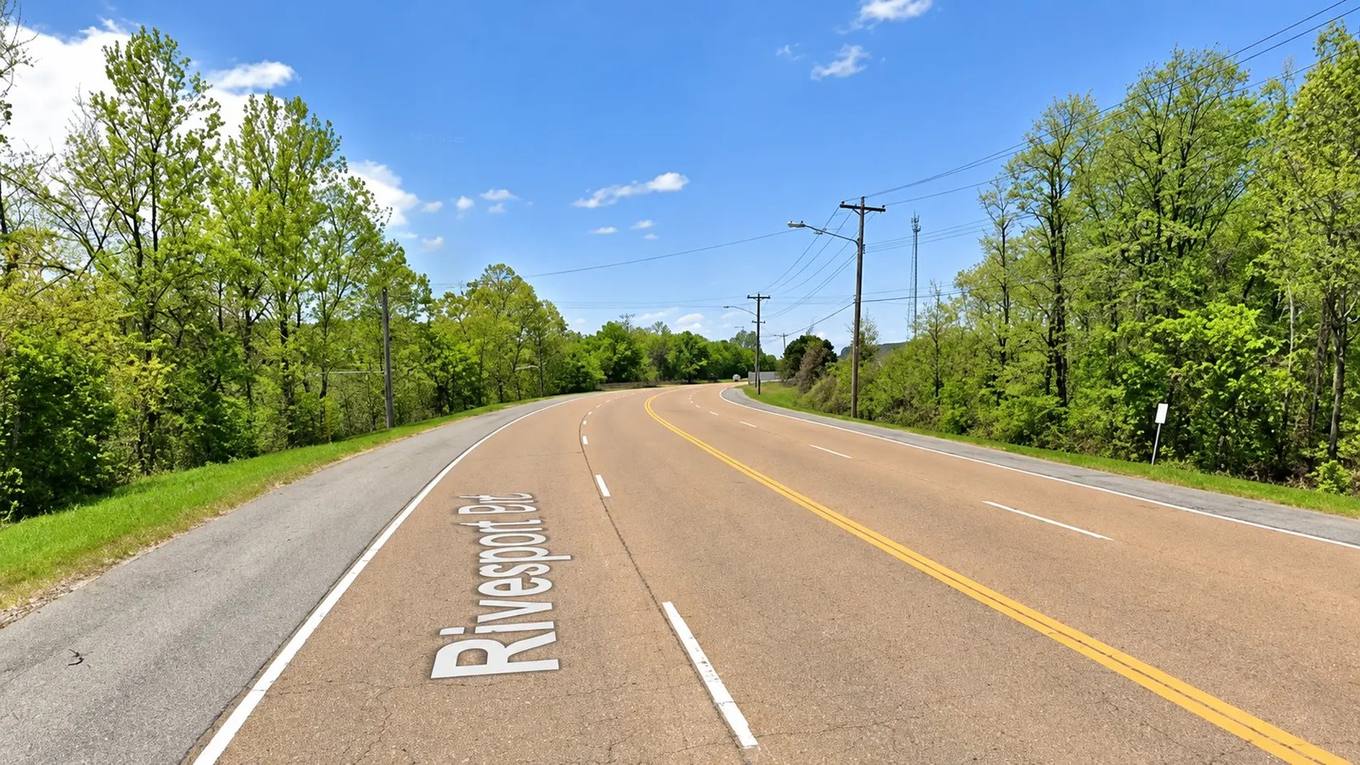 A curving roadway labeled Riverport Road, lined with trees and utility poles under a blue sky.