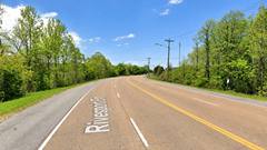 A curving roadway labeled Riverport Road, lined with trees and utility poles under a blue sky.