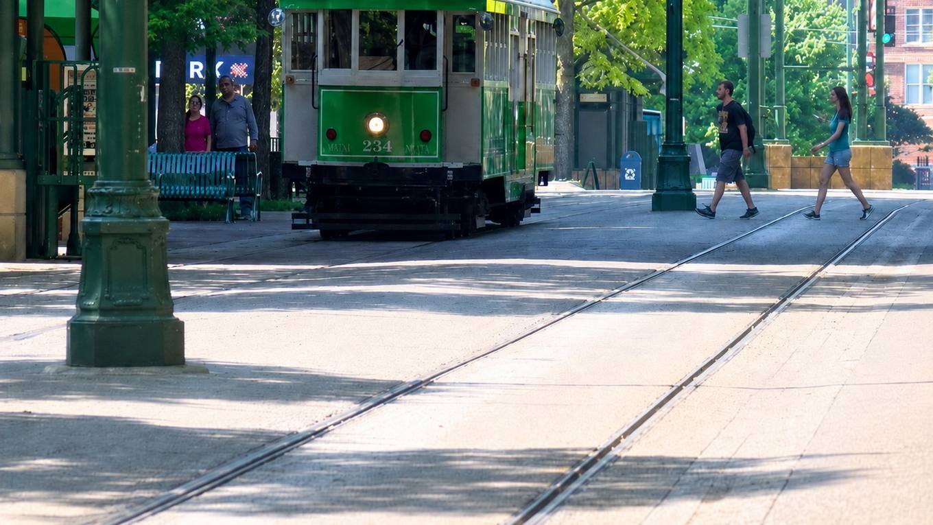 Empty streetcar rails set into a downtown street at early morning with overhead trolley wire above, representing the suspended trolley service.