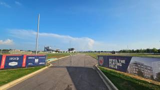 An empty, fenced urban development parcel with a stadium visible in the distance under overcast daylight.