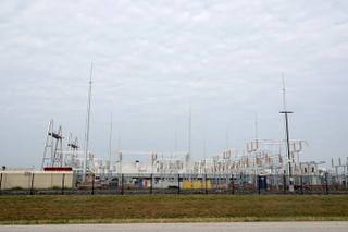 A large windowless industrial data center building behind fencing with power lines overhead.