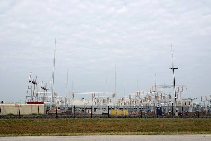 A large windowless industrial data center building behind fencing with power lines overhead.
