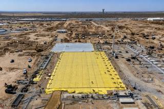 Aerial view of a large data center construction site, with a yellow vapor barrier and rebar mat covering a freshly prepared foundation pad surrounded by graded earth and heavy equipment.