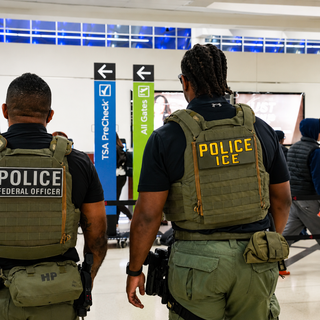 Federal immigration officers in tactical vests stand inside an airport terminal concourse.