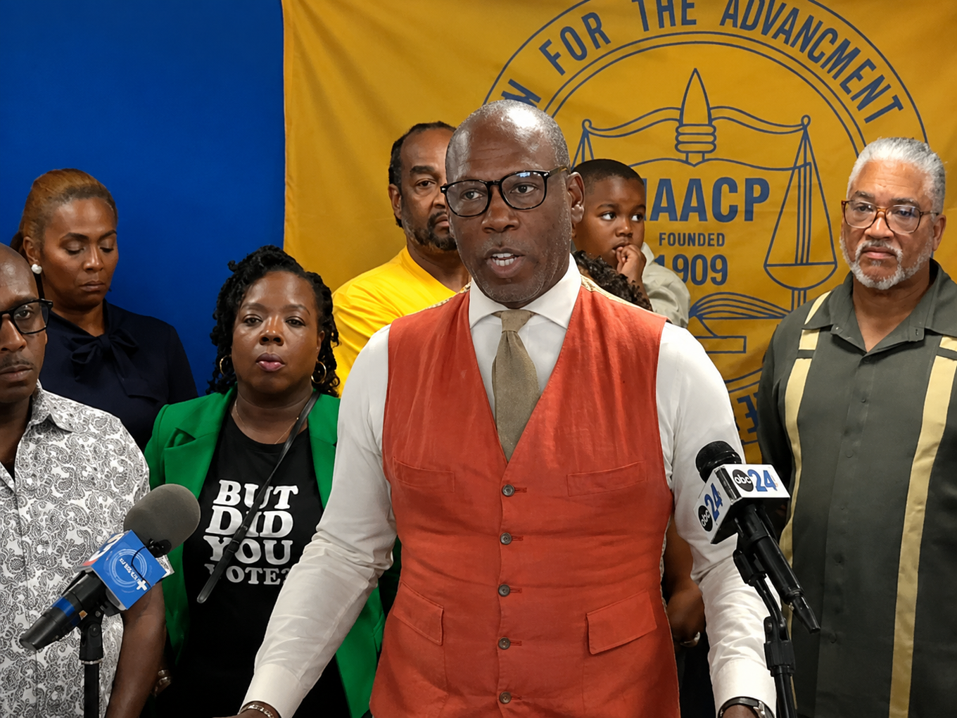 NAACP Memphis Branch President Kermit Moore speaks at a press conference in front of an NAACP banner, with community members standing behind him.