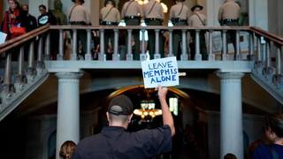 A protester holds a Leave Memphis Alone sign as Tennessee state troopers stand on the Capitol staircase.