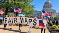 Demonstrators hold a Fair Maps banner outside a state capitol building under a clear sky