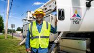 A Memphis Light, Gas and Water technician stands beside an MLGW bucket truck on a Memphis roadside in summer light.