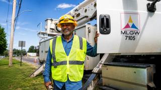 A Memphis Light, Gas and Water technician stands beside an MLGW bucket truck on a Memphis roadside in summer light.