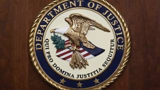 The seal of the United States Department of Justice mounted on a wood-paneled wall.