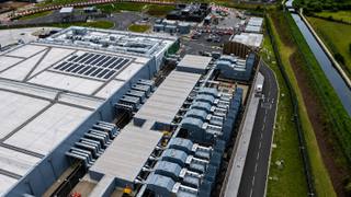 Aerial view of a large data center campus with rows of backup generators and cooling units alongside an on-site electrical substation.