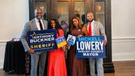 Shelby County Sheriff-elect Anthony J. Buckner and Mayor-elect Mickell M. Lowery hold campaign signs with Chrystal Buckner and Chonisa Lowery at an indoor reception.