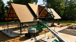 A nearly finished public park pavilion under construction, with new steel framing and roof decking, a lift on site and fresh concrete walkways.