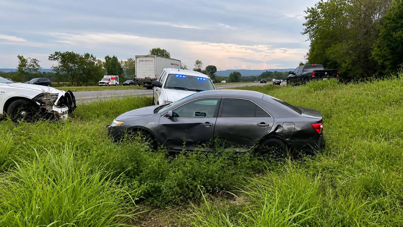 Two damaged cars in the grass beside a Tennessee highway with a patrol vehicle and ambulance responding