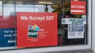 A red "We Accept EBT" sign displayed in a grocery store window, beside a "Food Stamps Accepted" notice.