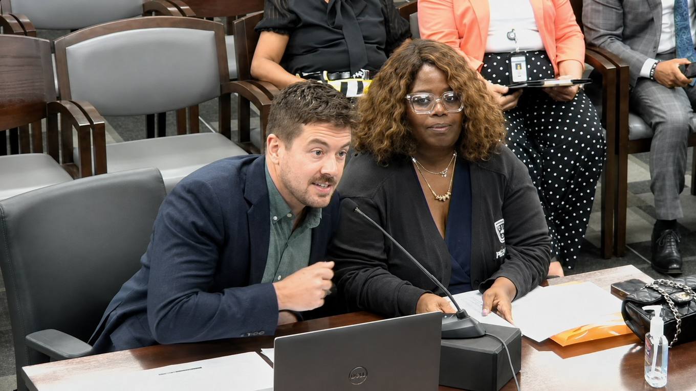 Two officials seated at a witness table with a laptop and papers speak into a microphone during a Memphis City Council committee meeting.
