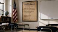 A sunlit classroom with a framed Ten Commandments poster on the wall beside an American flag and rows of empty desks.