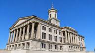 The Tennessee State Capitol in Nashville, with its columned facade, cupola, and flag under a clear blue sky.