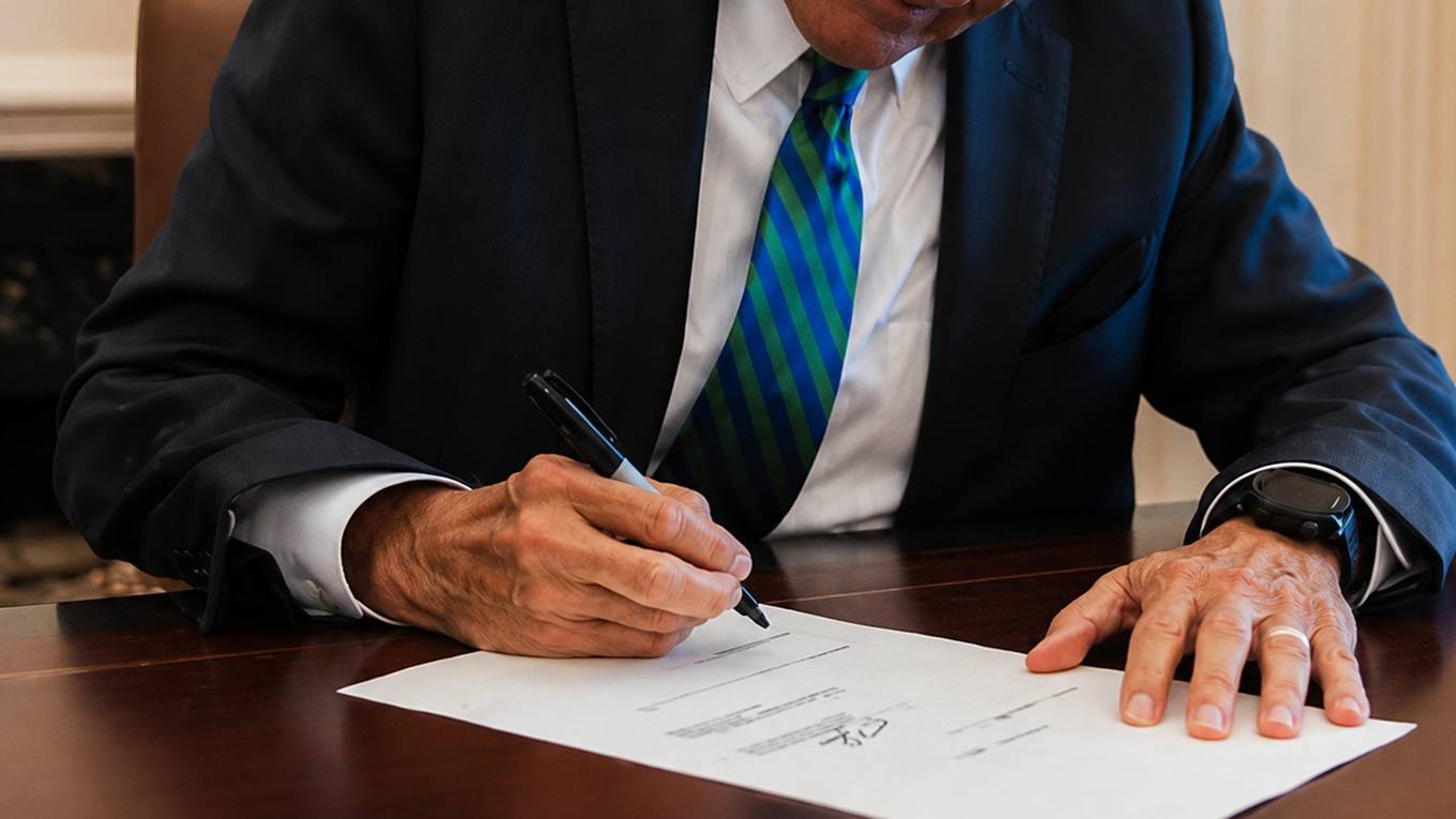 Governor Bill Lee signs a document at a desk with the Tennessee state flag behind him.