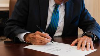 Governor Bill Lee signs a document at a desk with the Tennessee state flag behind him.
