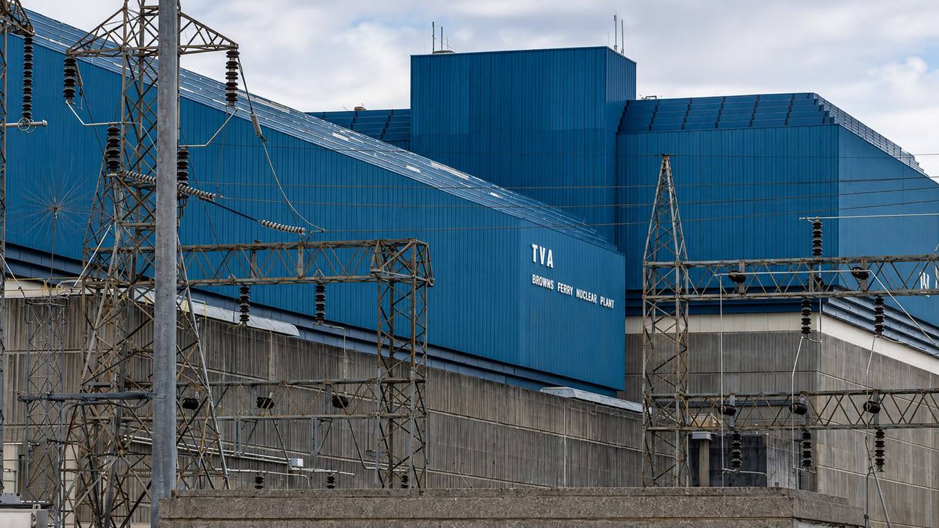 The blue reactor buildings of TVA's Browns Ferry Nuclear Plant behind steel transmission towers and power lines.