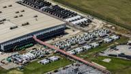 Aerial view of a large data center campus with rows of generators, cooling units and a substation on its perimeter.